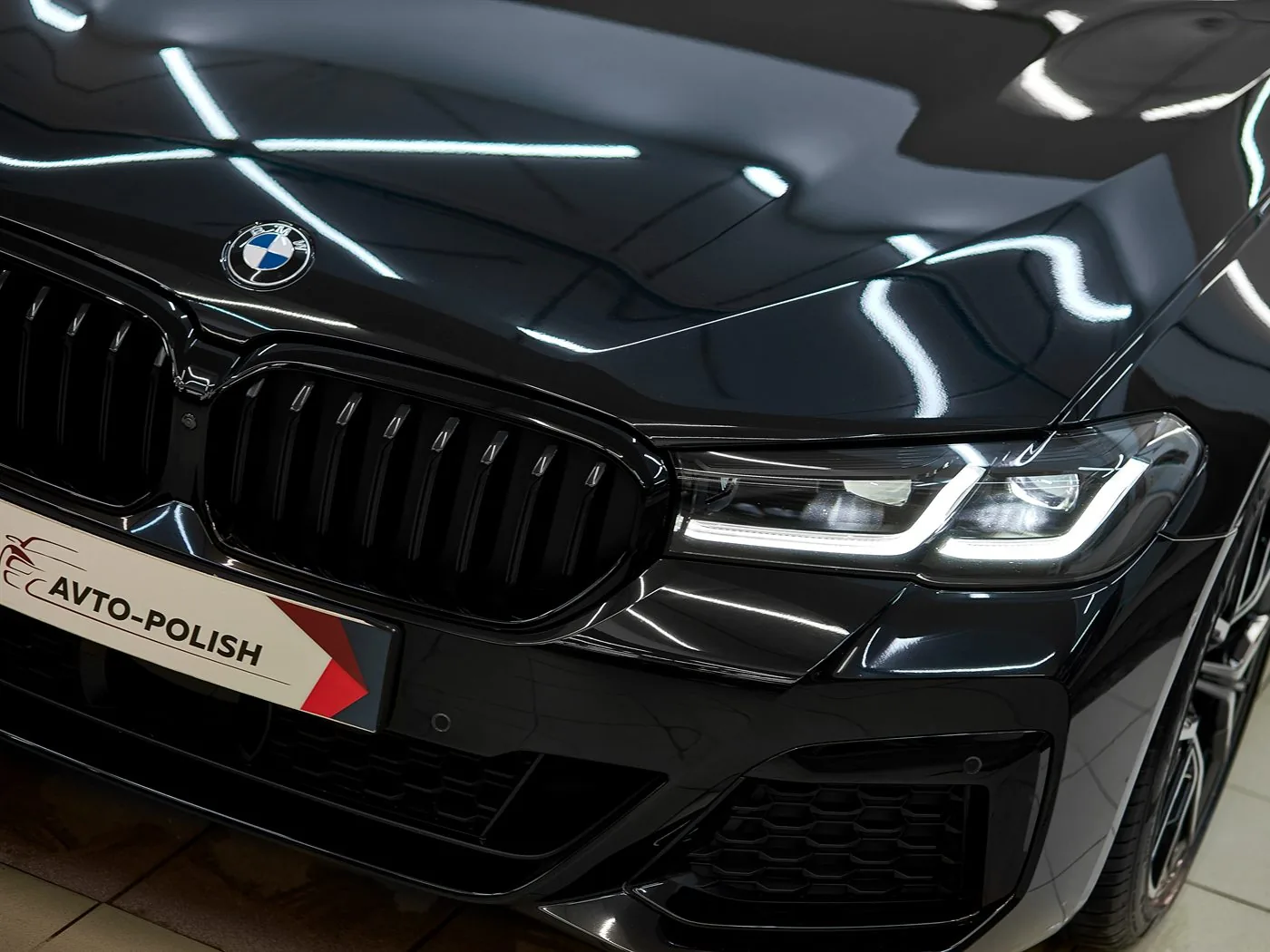 Чёрный BMW 5 после керамики: в лаке зеркально отражаются лампы цеха